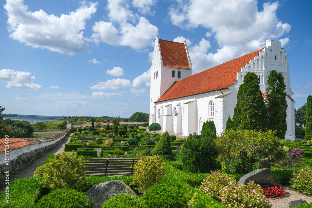 Fototapeta premium Fanefjord Kirke auf Møn mit Kirchengelände und Blick auf das Wasser des Fjords