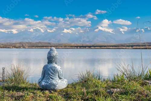 A statue of Buddha standing on the shore of a lake and meditating. In the distance is a snowy mountain. Meditation concept.