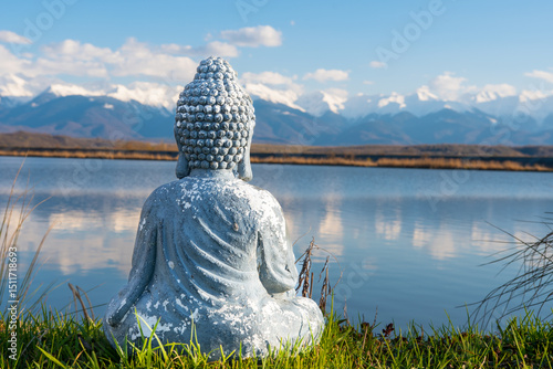 A statue of Buddha meditating standing on a lake shore. In the distance is a snowy mountain. Meditation concept.