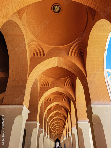 Symmetrical Islamic architectural hallway with elegant brick arches and domes, featuring traditional geometric design under warm lighting and a glimpse of blue sky.