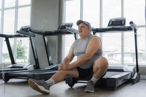 An overweight man is experiencing knee pain while exercising on a treadmill in a gym.