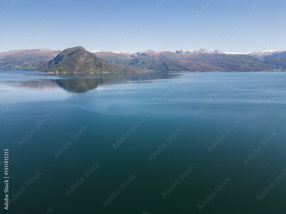 Nature of Norway, photo drone view: serene Hardangerfjord, blue waters and mountain ranges under a clear sky. Nature of Norway, photo drone view: serene Hardangerfjord, blue waters and mountain ranges under a clear sky.