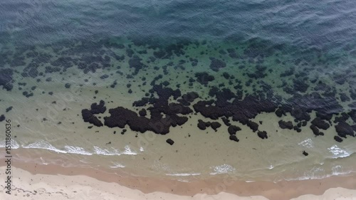 Turquoise waters lapping sandy shore, black volcanic rocks gleaming under bright sunlight, pristine ocean waves rolling softly