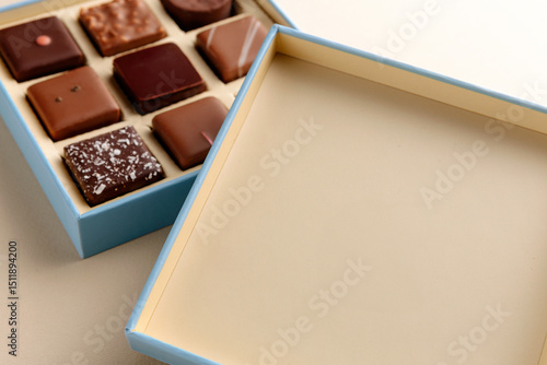 Minimal overhead shot of open box with chocolate squares on beige background, elegant candy dessert packaging mockup concept