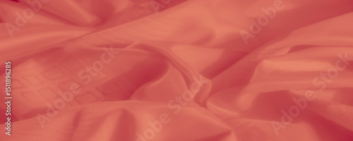 The fabric in a beautiful coral tone lays gently, with soft, flowing curves and a refined texture. Its surface reflects light in a way that highlights its woven detail and softness.