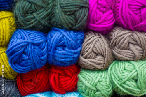 Colorful yarn balls neatly stacked, featuring vibrant pink, blue, red, green, and yellow hues. The soft textures create a cozy and inviting scene.