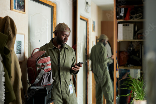 African American man in a uniform standing in hallway holding smartphone and looking down, getting ready to leave home and go to work