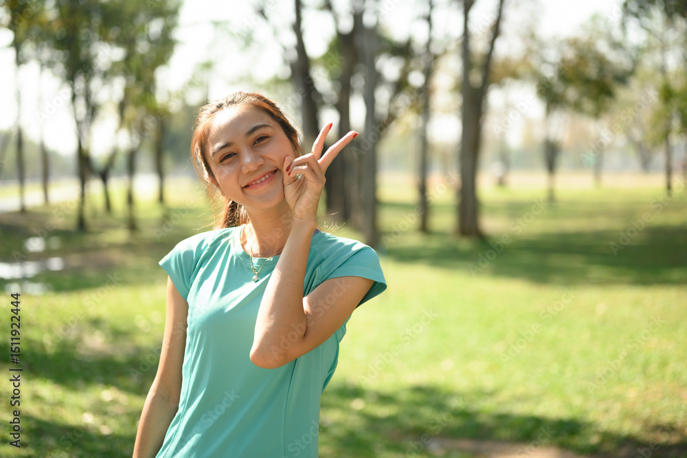 Young Asian woman smiling brightly and showing a peace sign with her fingers while enjoying a sunny day in a green park Young Asian woman smiling brightly and showing a peace sign with her fingers while enjoying a sunny day in a green park