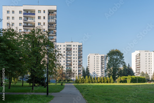 A large public park with a green lawn and trees located in a high-density housing estate. A walking path winds through this recreational space, with tall blocks of flats in the background.