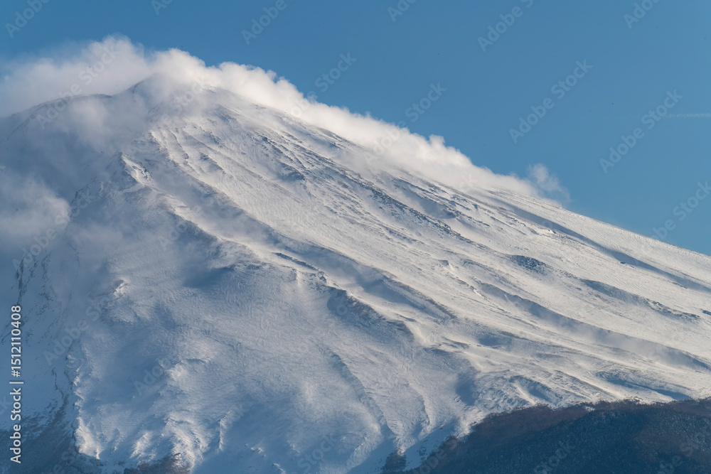 Fototapeta premium Close up of snow covered symmetrical cone of active stratovolcano Mt. Fuji with some cloud flurries over the top of the volcano