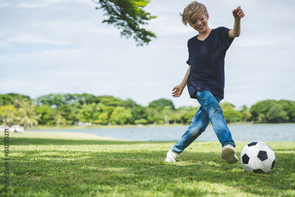 Obraz premium Little boy playing football in the garden with morning sunrise