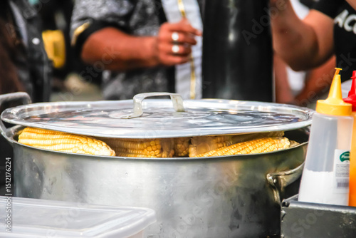A large metal cooking pot filled with boiling liquid and corn is used during outdoor food preparation. The scene captures traditional large-scale cooking methods commonly used at festivals.