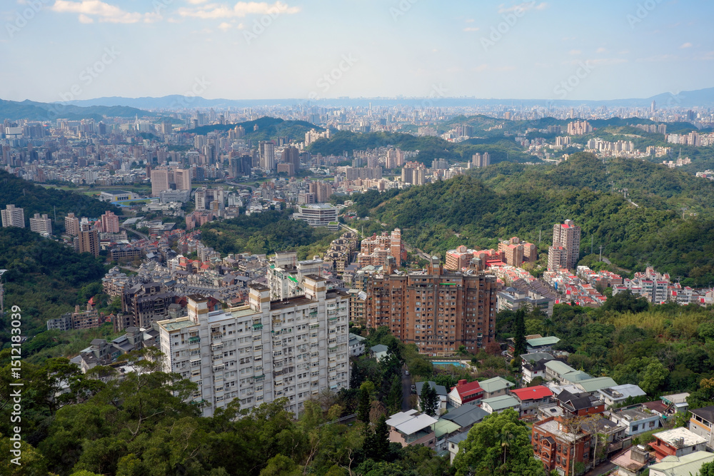 Fototapeta premium Panoramic view of a sprawling city with numerous buildings nestled among lush green hills under a clear sky, showcasing urban development and natural landscape.