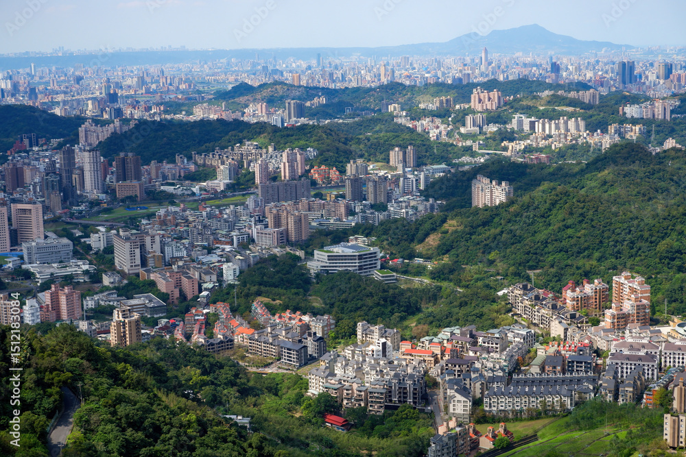 Fototapeta premium Panoramic aerial view of a sprawling city nestled among lush green hills and mountains under a clear sky, urban landscape.