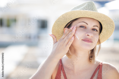 Woman applying sunscreen on her face by the beach on a sunny day