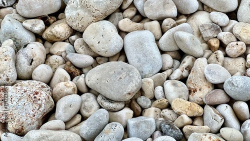 Smooth sea pebbles cover the shore in a natural coastal pattern. Beach texture, marine background, nature detail, seaside calm, minimalist composition, ocean shore, relaxation, travel mood. 