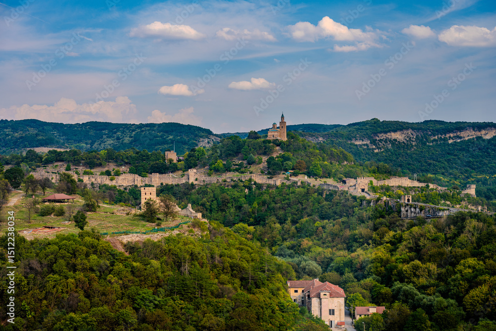 Fototapeta premium Wide View of Tsarevets Fortress Surrounded by Forested Hills and Ancient Walls in Veliko Tarnovo, Bulgaria under a Partly Cloudy Sky