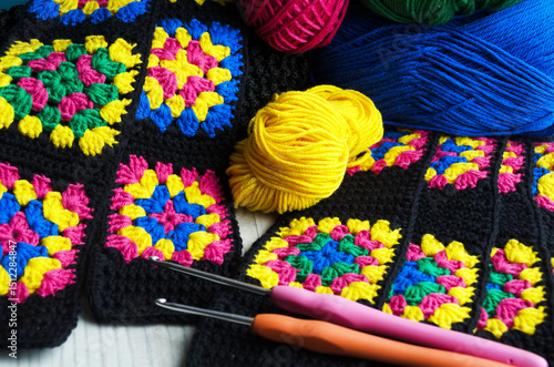 A vibrant crochet project featuring black squares with colorful granny square centers in pink, yellow, blue and green.