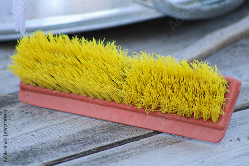 A yellow broom with a red handle set on a wooden surface, with its bristles neatly arranged. The contrasting colors and textures add depth to the scene	
