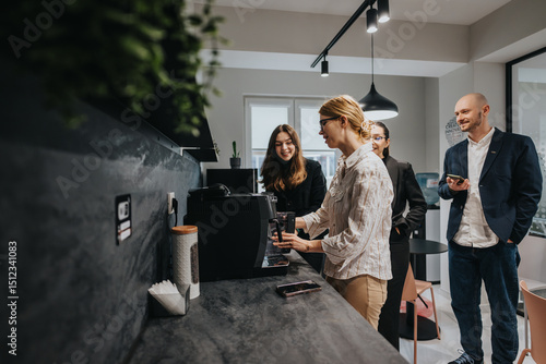 Obraz na płótnie A group of business colleagues gather around a coffee maker, sharing smiles and conversation during a break in a modern, well-lit office space