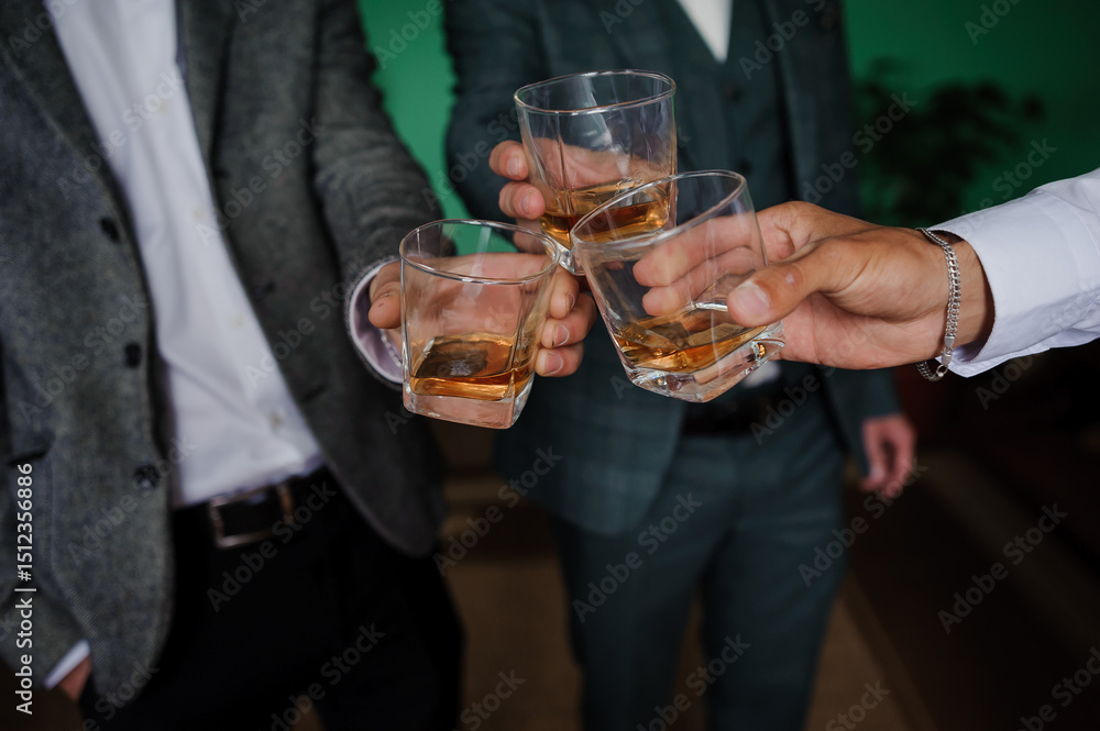 Three well-dressed men in suits raising glasses of whiskey in a celebratory toast during an elegant gathering, possibly a wedding or business event. Three well-dressed men in suits raising glasses of whiskey in a celebratory toast during an elegant gathering, possibly a wedding or business event.