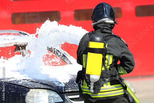 Firefighter with oxygen tank while spraying extinguishing foam to put out the fire that broke out in the car after the road accident