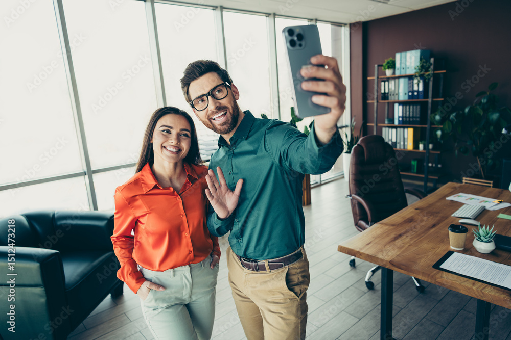 Obraz premium Two smiling coworkers in a modern office taking a selfie, showcasing teamwork and a collaborative corporate environment.