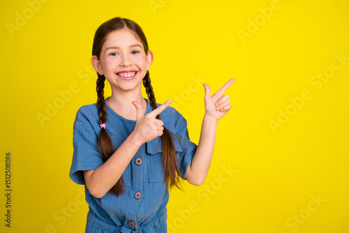 Fotografija Charming young girl with braided hairstyle pointing happily on bright yellow bac