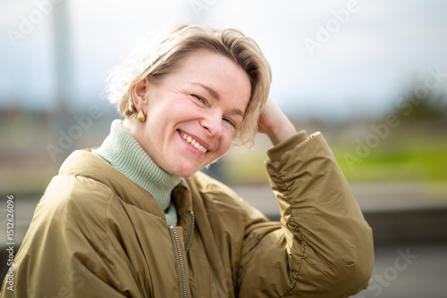 Woman with short blond hair smiling confidently outdoors on a sunny day