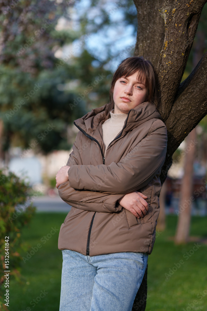 portrait of a teenage girl in a spring park, stands leaning against a tree portrait of a teenage girl in a spring park, stands leaning against a tree