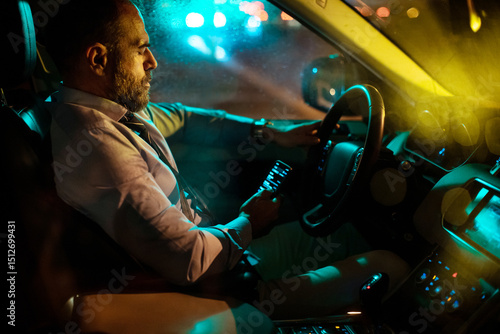 Sleepy distracted and tired middle aged caucasian businessman driving a car at night and using his phone