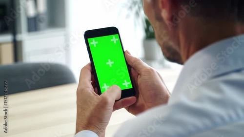Man holding smartphone with green screen for chroma key compositing and digital content integration in a modern office setting