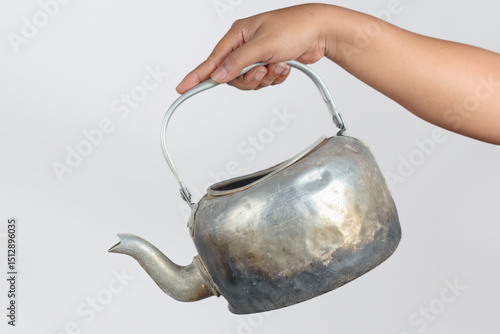 Old aluminum kettle held by hand with scorched base and curved spout
