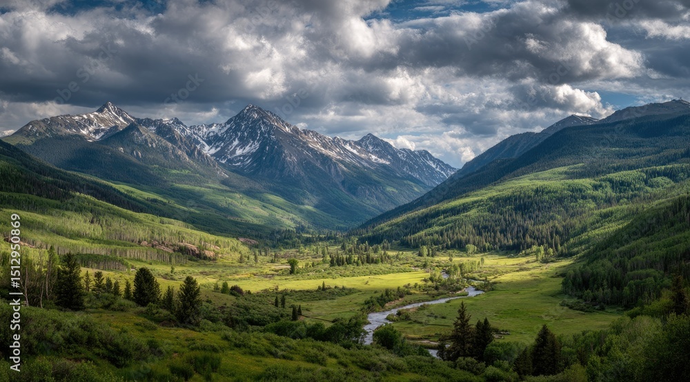 Obraz premium Panoramic view of a verdant valley nestled between snow-capped mountains under a dramatic, partly cloudy sky.