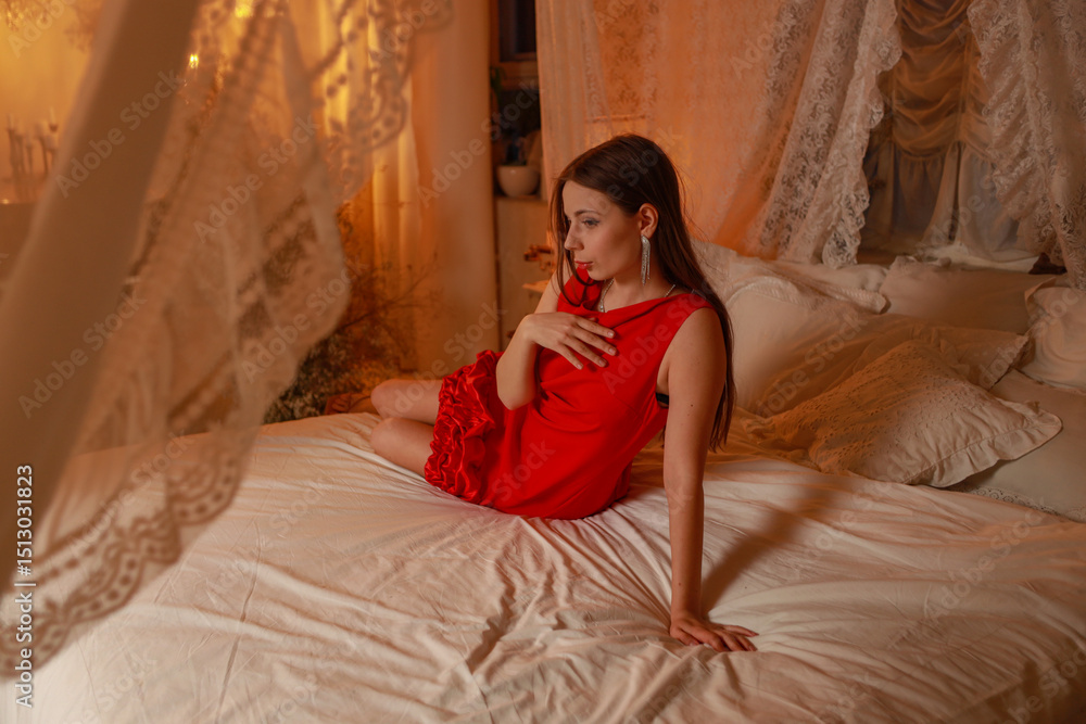 Fototapeta premium Young slim pretty brunette woman in red dress lying on bed in vintage bedroom