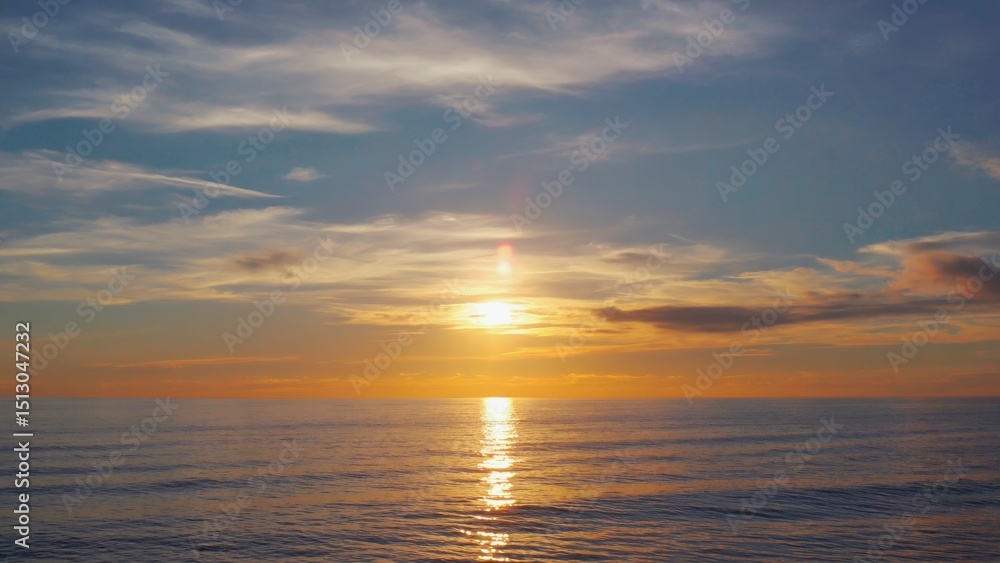 The sky is blue and the sun is setting. The water is calm and the horizon is visible The sky is blue and the sun is setting. The water is calm and the horizon is visible
