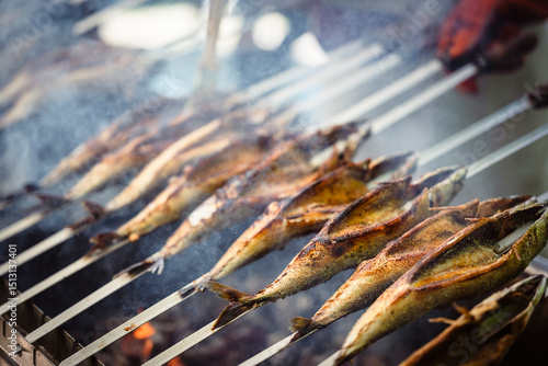 Steckerlfische - Fische auf Metallspießen - werden über Holzkohle auf einem Fest in Bayern gegrillt