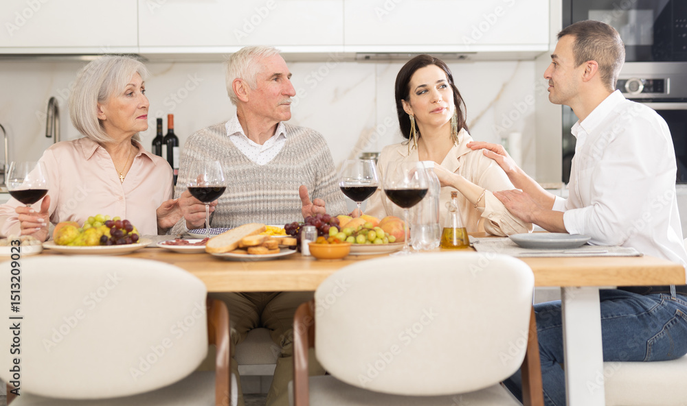 Mature couple are sitting at table with younger spouses friend, drinking wine and enjoying snacks, chatting merrily, raise glass to, celebrating important event. Mature couple are sitting at table with younger spouses friend, drinking wine and enjoying snacks, chatting merrily, raise glass to, celebrating important event.