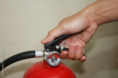 Hand squeezing the lever of a red fire extinguisher. Ready to discharge.
