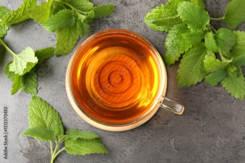 Fotografie Aromatic lemon balm tea in glass cup and fresh leaves on gray textured table, fl