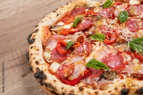 A close-up image of a wood-fired pizza topped with pepperoni, ham, red bell peppers