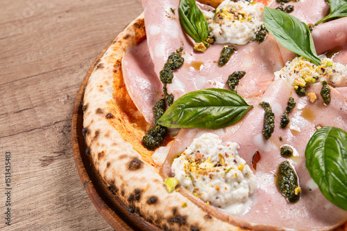 A close-up of a delicious Italian pizza featuring mortadella slices, ricotta cheese, basil leaves, pesto sauce,