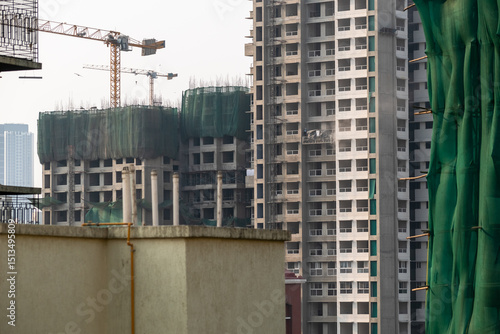 Construction activity is in full swing in Mumbai as cranes lift materials and workers manage various tasks on high-rise buildings.