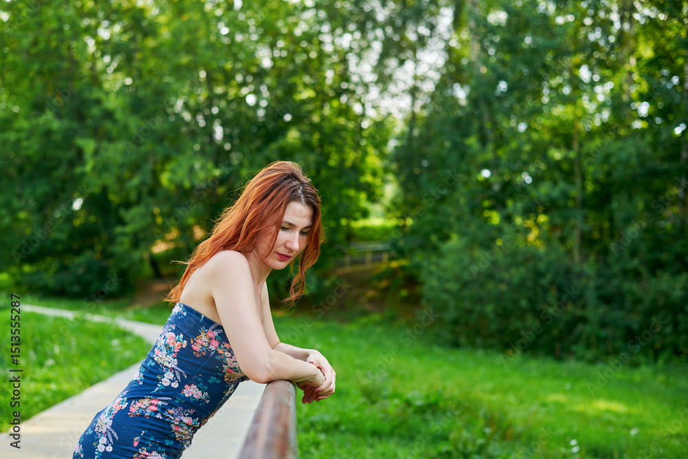 Woman in blue dress leaning on bridge railing in park. Relaxation and rest concept as woman enjoying her time outdoors. Lush green surroundings. Girl has beautiful body. Woman in blue dress leaning on bridge railing in park. Relaxation and rest concept as woman enjoying her time outdoors. Lush green surroundings. Girl has beautiful body.