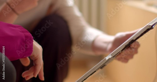 Two people share ideas on a tablet, pointing at the screen and engaging in a lively conversation. The closeup of their hands highlights the connection technology fosters in collaboration