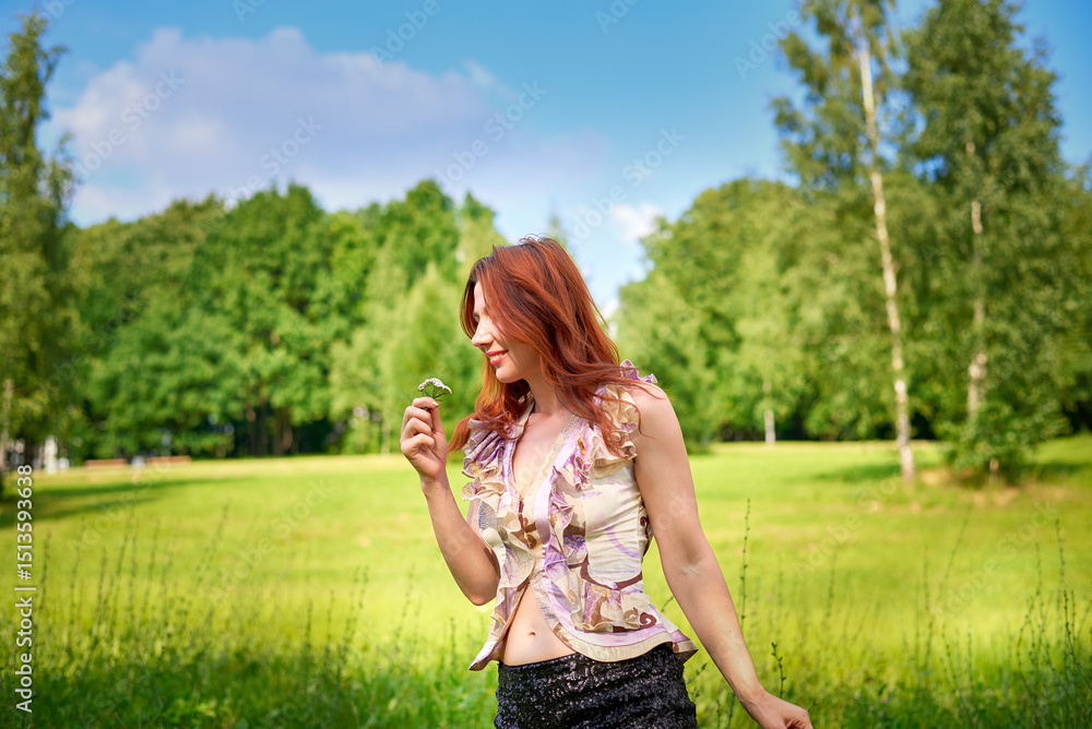 Obraz premium A woman in a pink shirt and black shorts stands in a field in a park on a summer day. She poses for a photograph, and the mood of the image is light and carefree.