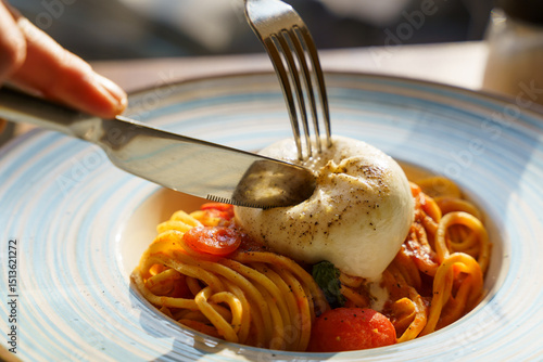 Cutting into burrata on spaghetti with tomato sauce