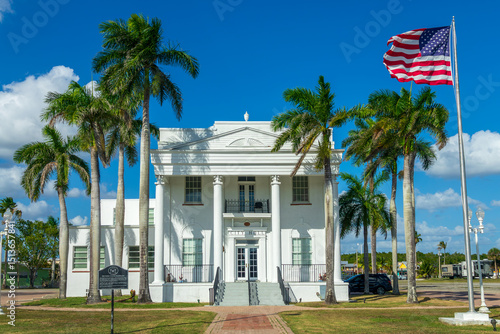 View of the City Hall of Everglades City located in the historic building of the Old Collier County Courthouse with palm trees and a US fllag, Florida