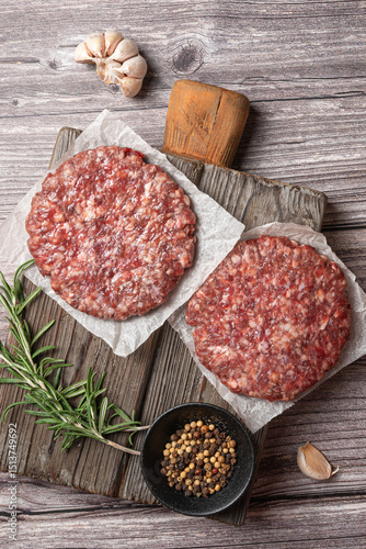 Two raw burger patties with spices and herbs on parchment and rustic cutting board. Flat lay food composition.