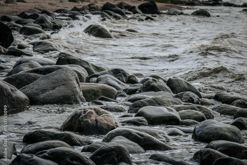 Obraz premium Ocean wave splashes over a dark coastal rock, capturing motion and texture in the clear water under cloudy skies.